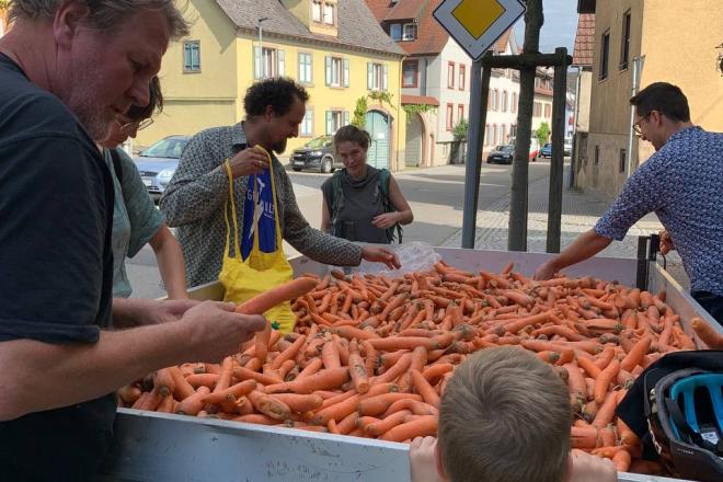 Teilnehmer*innen stehen um einen Anhänger mit Mohrrüben