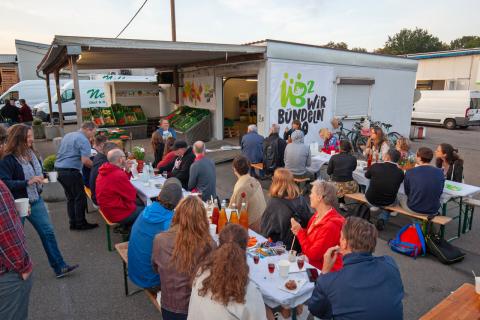 Menschen sitzen während der Einweihungsfeier des Regio-Bio-Containers auf dem Freiburger Großmarkt