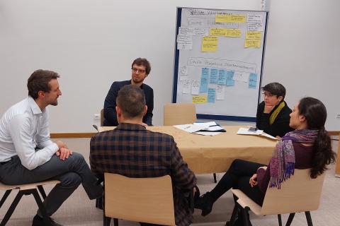 Fünf Teilnehmende sitzen an einem Tisch und disktuieren